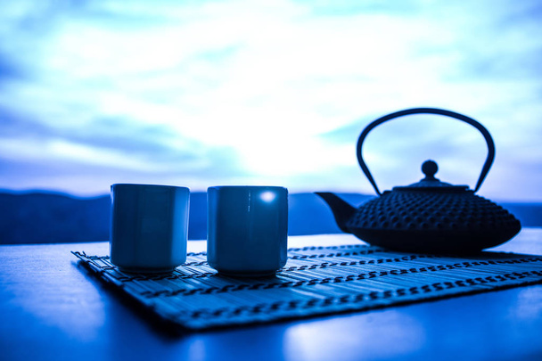 Tea concept. Japanese tea ceremony culture east beverage. Teapot and cups on table with bamboo leaves on sunset - Foto, Imagen