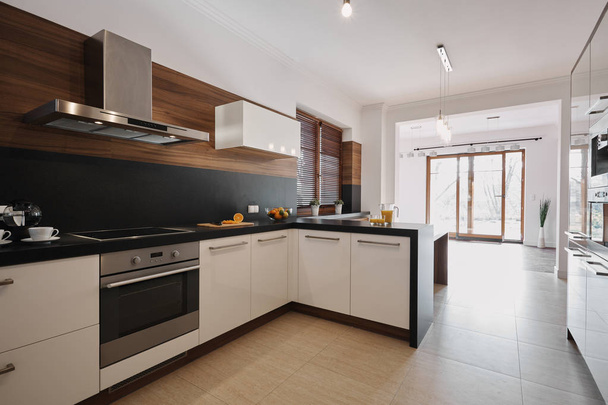 elegante weiße und schwarze Küche mit hölzernen Akzenten und offenen Raum leer Wohnzimmer Innenraum mit bodentiefen Fenstern - Foto, Bild