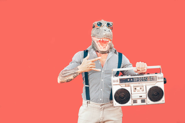 Homem sênior louco vestindo máscara t-rex enquanto ouve música segurando boombox vintage estéreo ao ar livre - Moda mascarada masculino se divertindo dançando e celebrando - Absurdo e conceito de pessoas engraçadas
 - Foto, Imagem