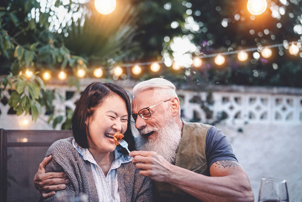 Happy senior couple having fun at dinner house party - Older people with different ethnicity doing a romantic date for celebrating anniversary - Elderly, food, drink and love concept - Fotoğraf, Görsel