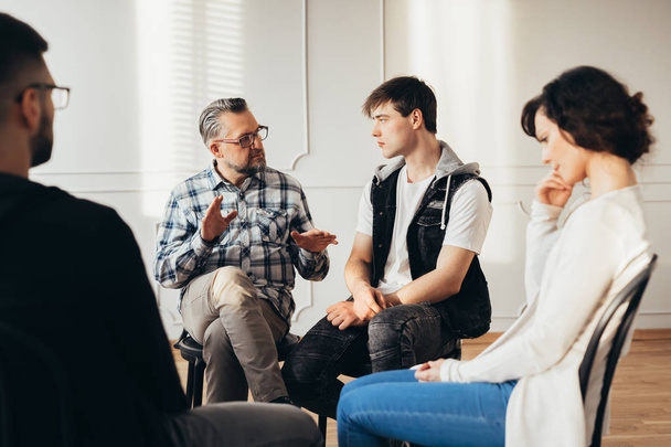 Psychologist talking about twelve-step program to addicted man during group support meeting - Photo, image