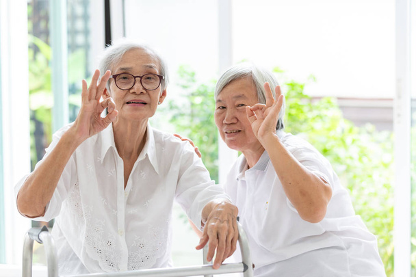 Щасливі дві азіатські літні жінки, показуючи знак з рукою і пальцями разом, відмінний символ,друзі літньої жінки або сестри посміхаються позитивно з ходунком,дружба літніх людей, пенсійний вік
 - Фото, зображення