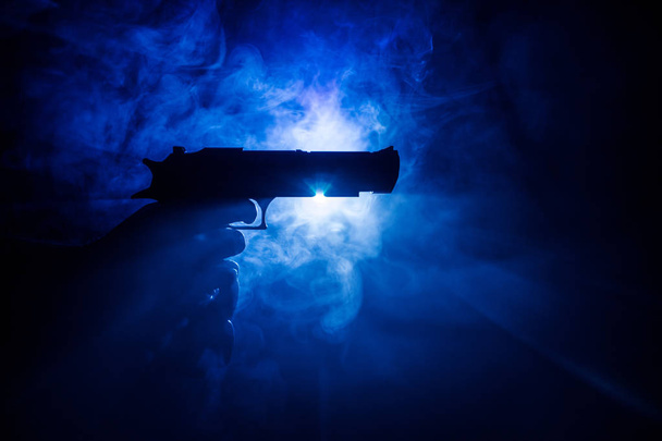 Male hand holding gun on black background with smoke toned back lights - Photo, Image