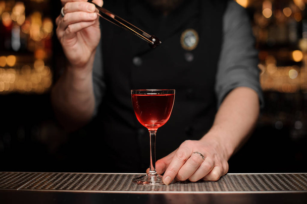 Male bartender adding a one red berry with tweezers to the cocktail - Fotó, kép