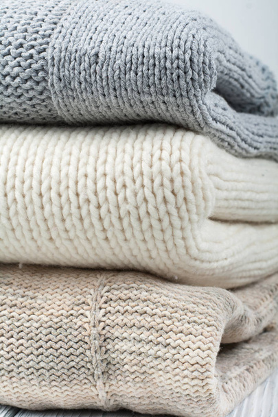 Knitted wool sweaters. Pile of knitted winter clothes on wooden background, sweaters, knitwear, space for text. - Zdjęcie, obraz
