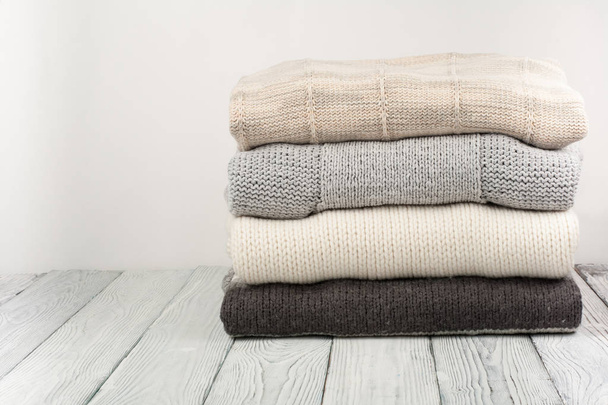 Knitted wool sweaters. Pile of knitted winter clothes on wooden background, sweaters, knitwear, space for text. - Photo, image