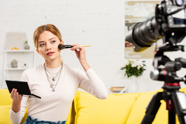 Blogger piękno siedzi na żółtej kanapie i robi makijaż przed kamerą wideo - Zdjęcie, obraz
