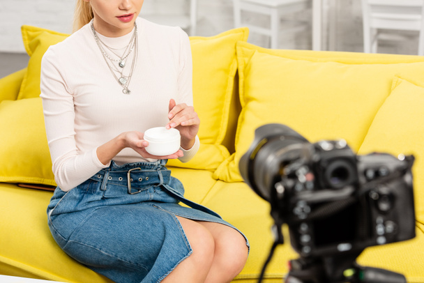vue recadrée du blogueur en jupe en denim tenant crème cosmétique devant la caméra vidéo
 - Photo, image