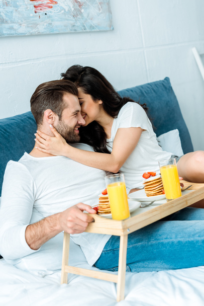 woman gently hugging man with breakfast on wooden tray in bed - 写真・画像