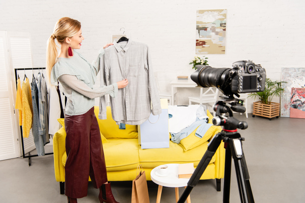 blogueiro sorrindo mostrando roupas na frente da câmera de vídeo em casa
 - Foto, Imagem