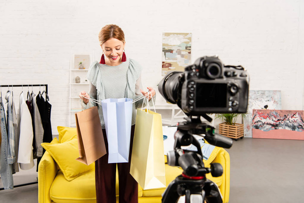 smiling blogger looking in shopping bag in front of video camera at home - Fotó, kép