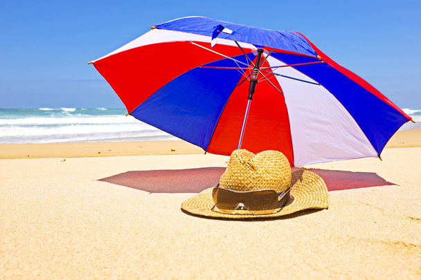 ψάθινο καπέλο, γυαλιά ηλίου και ομπρέλα στην παραλία - Φωτογραφία, εικόνα