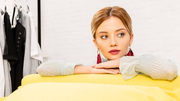 Nachdenkliches Mädchen mit Ohrringen sitzt zu Hause auf gelbem Sofa - Foto, Bild
