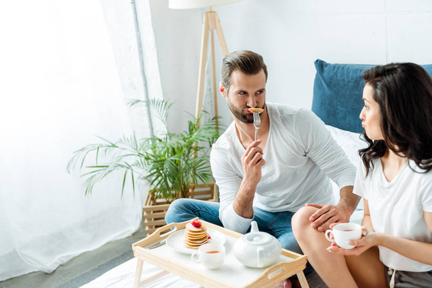 funny couple grimacing near wooden tray with breakfast in bed - Photo, Image