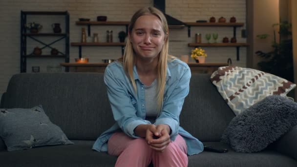 Young blonde woman sitting on the sofa and looking comedy film. Laughing, smiling. Looking at the camera. - Metraje, vídeo