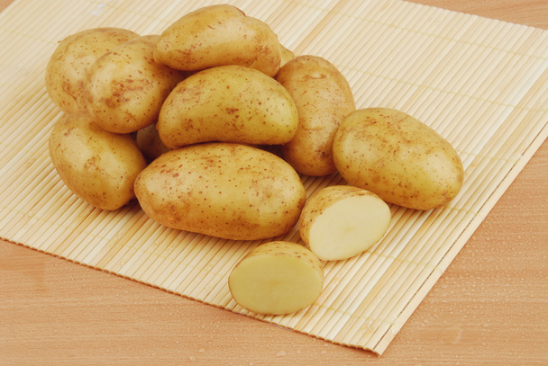 Lots of raw potatoes on bamboo stand on gray isolated background - Photo, Image