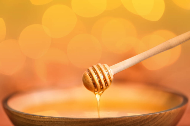 Honey dripping from dipper into bowl against blurred lights, closeup - Zdjęcie, obraz