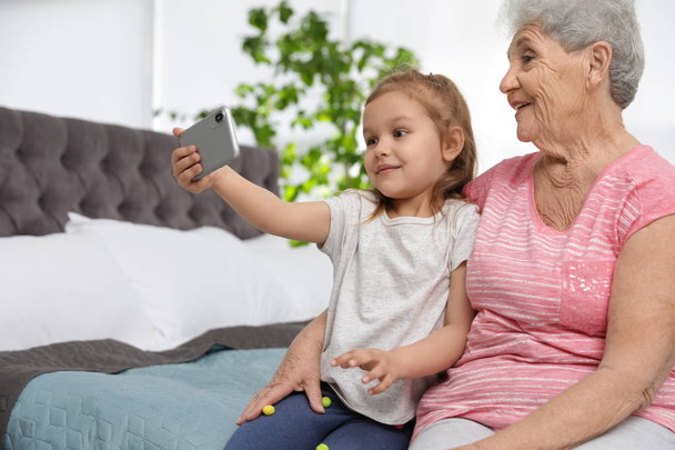 Cute girl and her grandmother taking selfie  at home - Фото, изображение