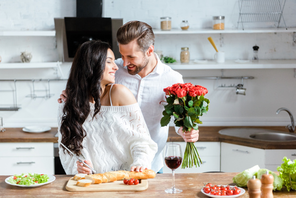 バラの花束を持っている男が夕食を調理する幸せなカップル - 写真・画像