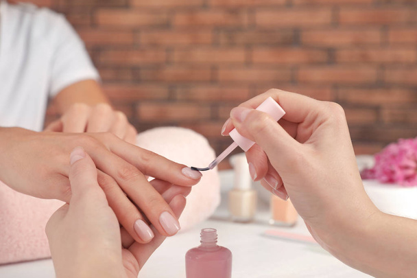 Manicurist applying polish on client's nails at table, closeup. Spa treatment - Foto, imagen