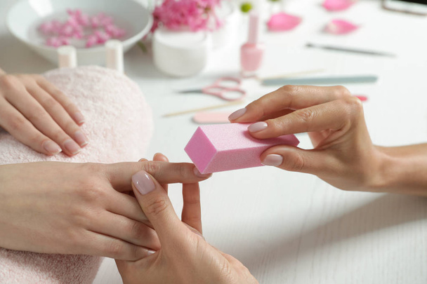 Manicurist polishing client's nails with buffer at table, closeup. Spa treatment - Zdjęcie, obraz