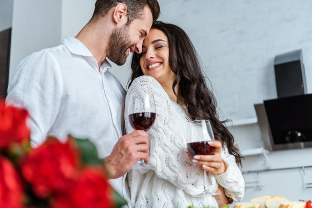 selective focus of happy couple holding glasses with red wine and looking at each other - Foto, Imagen