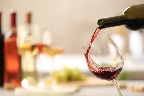 Pouring red wine from bottle into glass on blurred background. Space for text - 写真・画像