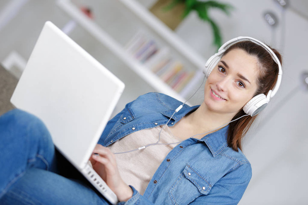 young lady at home wearing headphones plugged into her laptop - Zdjęcie, obraz