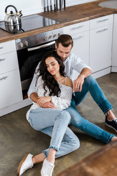 overhead view of couple sitting on floor and hugging at kitchen - Фото, зображення