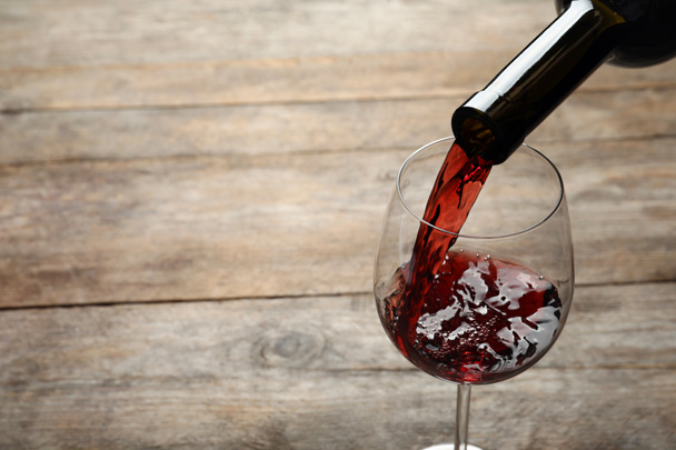 Выливание красного вина из бутылки в бокал на деревянном фоне. Пространство для текста
 - Фото, изображение