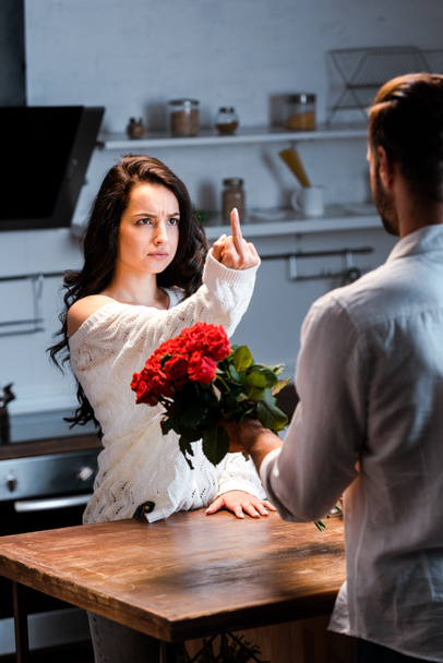 donna arrabbiata mostrando dito medio all'uomo con mazzo di rose rosse
  - Foto, immagini
