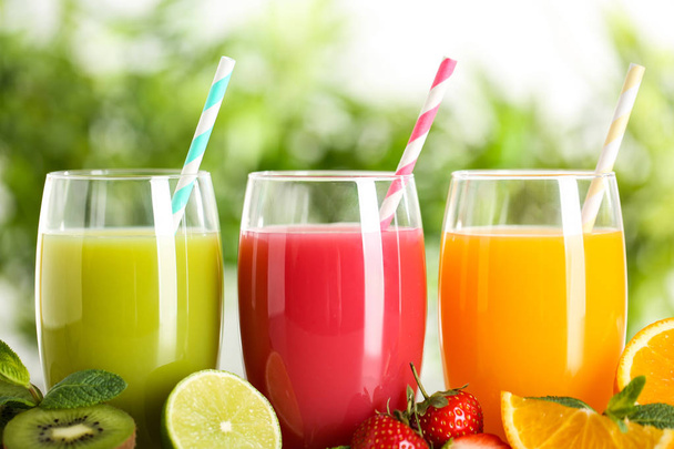 Glasses of different juices with straws and fresh fruits on blurred background - Foto, immagini