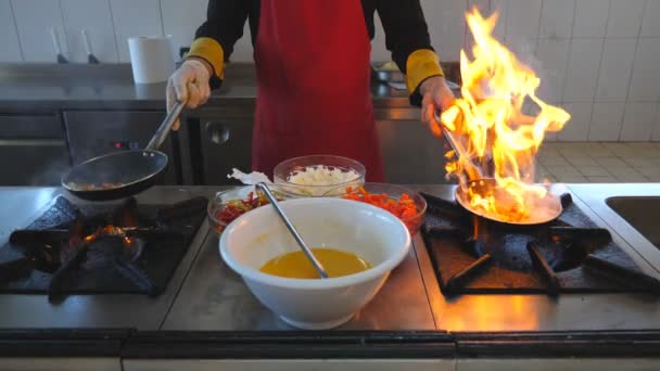 Onherkenbaar chef houdt twee pannen en koken flamberen stijl gerecht in moderne keuken van restaurant. Mannelijke kok gooien en bakken van groenten in pannen op kachel. Concept van het koken. Vooraanzicht Slowmo - Video