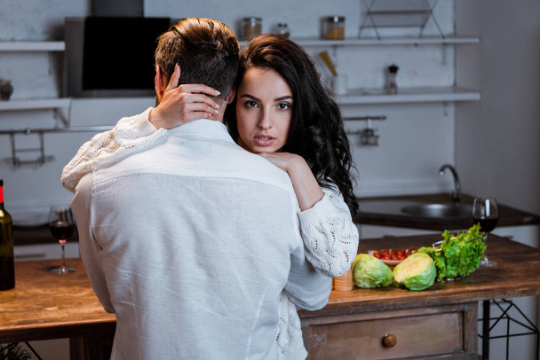 donna bruna appassionata abbracciando l'uomo e guardando la fotocamera in cucina
 - Foto, immagini