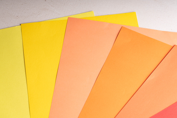 Φύλλα έγχρωμου χαρτιού είναι στο τραπέζι. Χαρτί από μπλε, κίτρινο, πράσινο, μπλε, κόκκινο, κοράλλια και ροδακινί χρώματα. Αφηρημένο δημιουργικό φόντο - Φωτογραφία, εικόνα