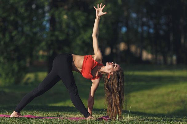 Young woman doing yoga exercises in the summer city park. Health lifestyle concept. - 写真・画像
