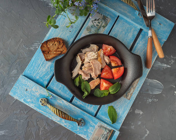 Light lunch of chicken and sliced tomatoes on a black ceramic plate. - Photo, Image