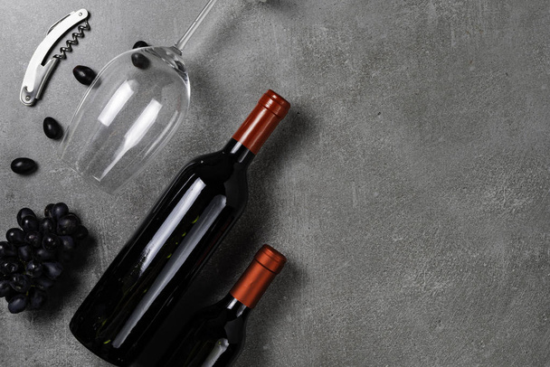 Butelki z winem, szkło, otwieracz i winogrona na betonowym tle. Przestrzeń kopiowania. - Zdjęcie, obraz