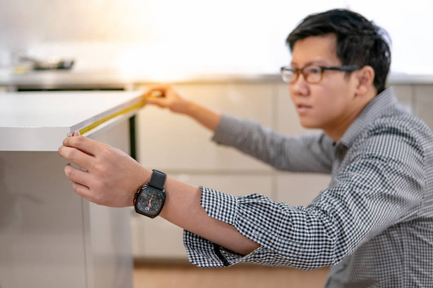 Азіатська людина, що використовує рулетка міра на кухні лічильник - Фото, зображення