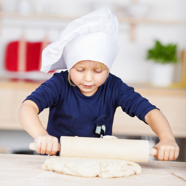 Little girl in a chefs hat rolling pastry - Photo, image