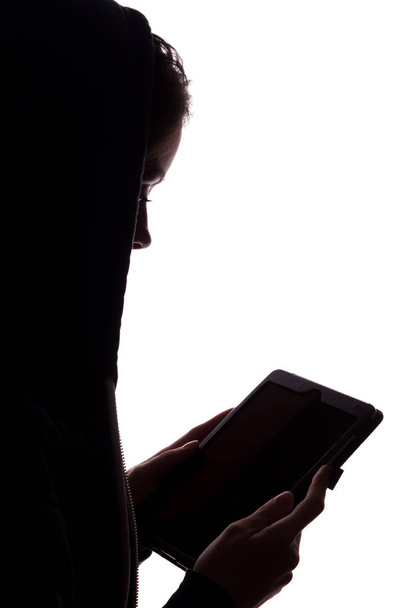 Silhouette eines Mädchens in der Kapuze mit einem Tablet - Foto, Bild