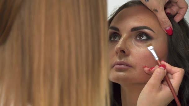 Makeup artist applies shadows to a woman's face with a brush. - Video, Çekim