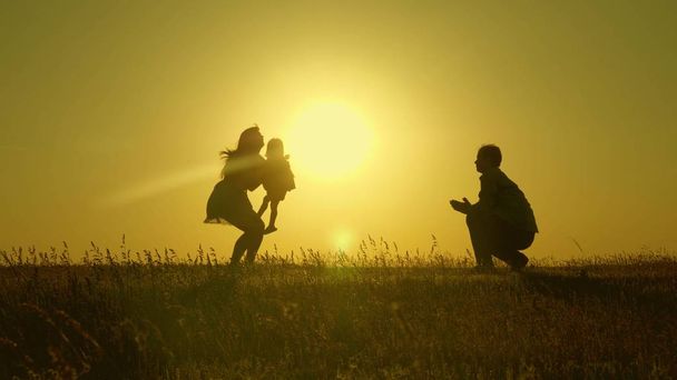 matka i tata bawią się z córką na słońcu. szczęśliwy dziecko idzie z tata do Mamo młodą rodzinę na polu z dzieckiem 1 rok. koncepcji szczęścia rodzinnego. piękne słońce, zachód słońca. - Zdjęcie, obraz