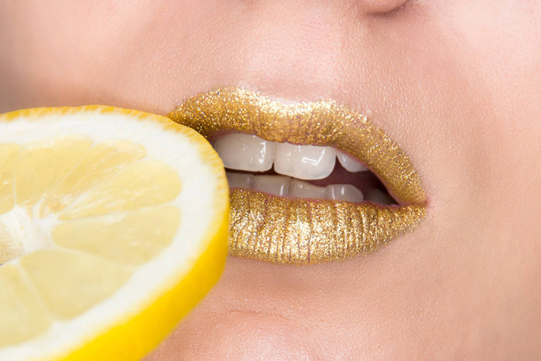 Hermoso primer plano con labios femeninos con maquillaje de color oro y rodaja de limón. Cosmética brillante
 - Foto, imagen