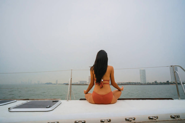 Young healthy and calm woman doing yoga meditation and sitting with lotus pose on sailing yacht boat - 写真・画像