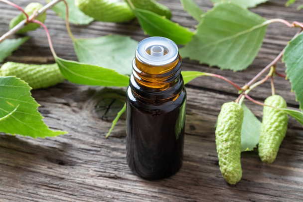 A dark bottle of essential oil with birch branches - Photo, Image