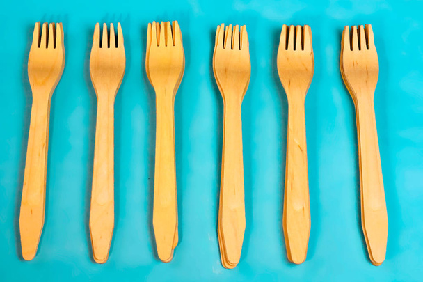 Disposable ecological wooden bamboo fork and spoon pattern on a blue background. Environment friendly flat lay with free copy space for text. Selective background - Photo, Image