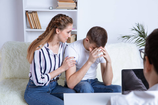 At the psychologist. Beautiful young couple is sitting on couch and hugging while doctor is making a note. - Photo, Image