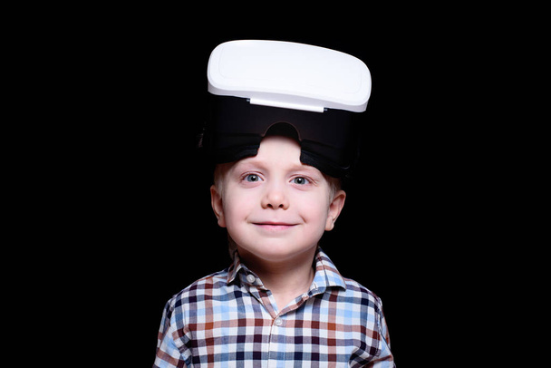 Kis mosoly fiú pohár virtuális valóság. Kockás póló. Fekete háttér - Fotó, kép