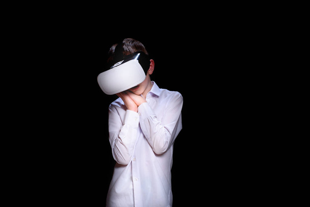 Jonge jongen met een virtual reality helm. Wit shirt. Zwarte achtergrond - Foto, afbeelding